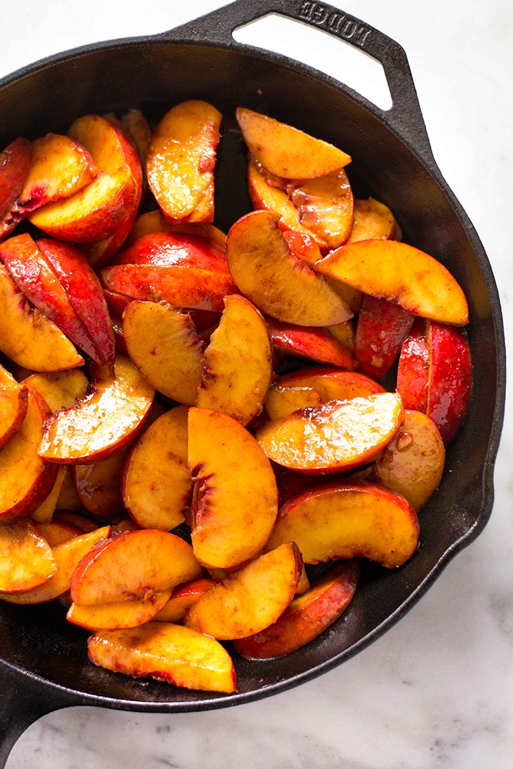Sliced fresh peaches, mixed with cinnamon, sea salt, and coconut sugar, and placed in a cast iron skillet, ready to be topped with biscuit cobbler topping.