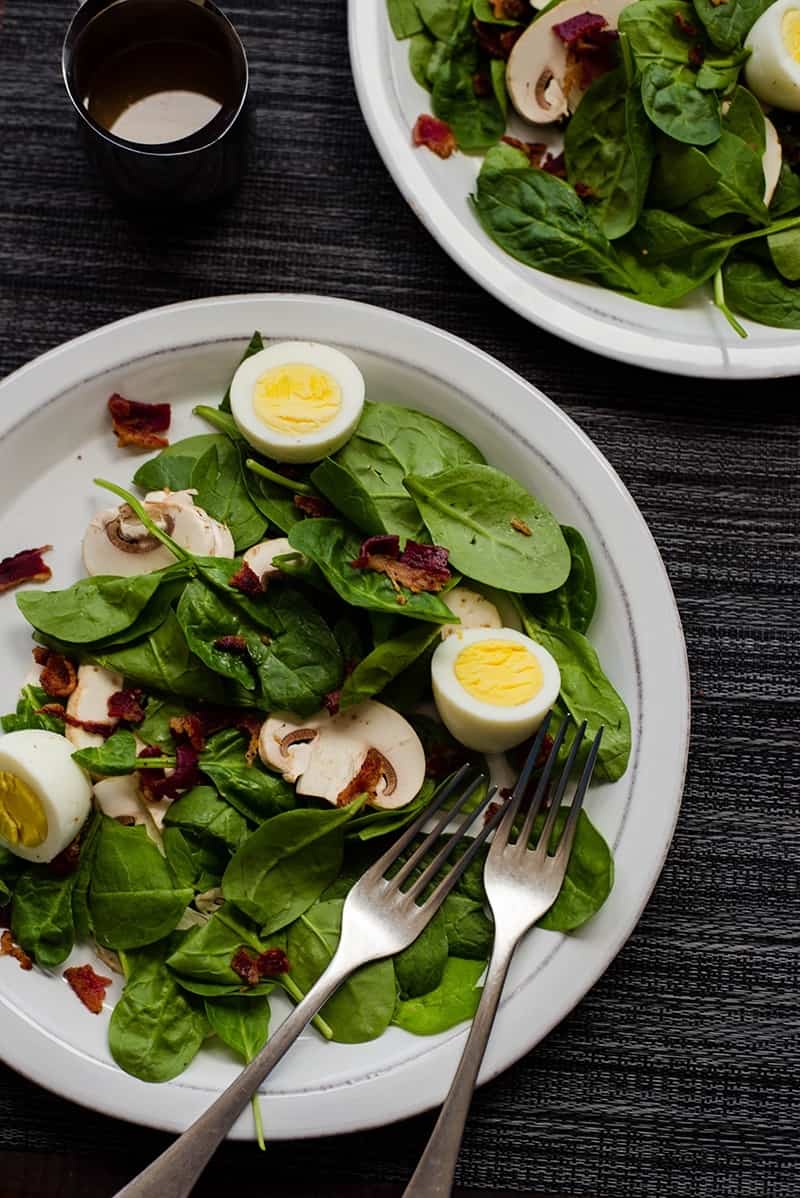 Overhead image of a plate of Spinach Salad With Warm Bacon Dressing, topped with bacon, mushrooms, and boiled eggs.