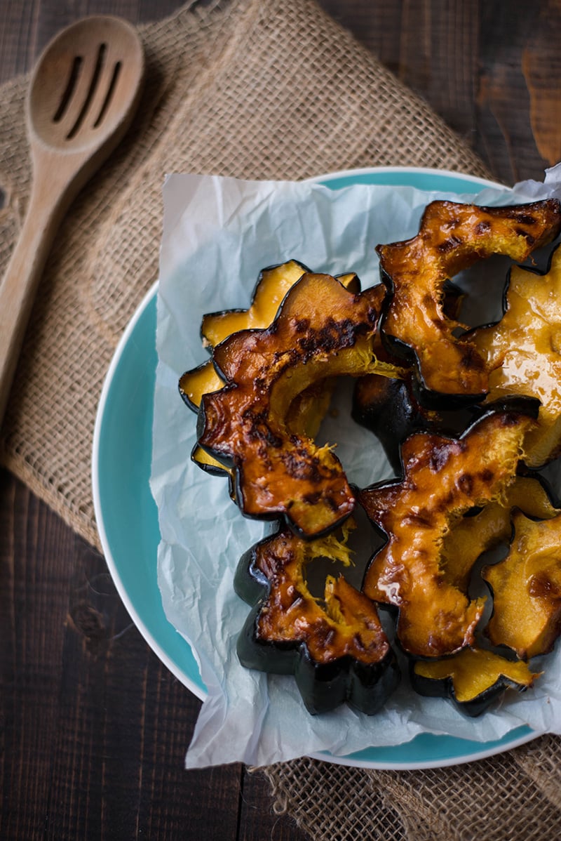 Overhead view of a blue plate filled with slices of Roasted Acorn Squash, with a serving utensil beside it.