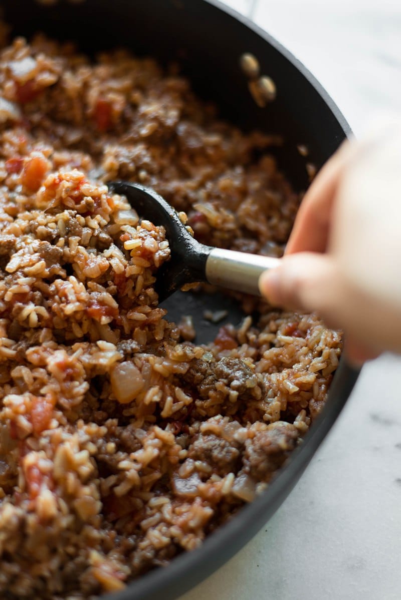 Deep skillet with mixture of lean ground beef, brown rice, onions, and tomato sauce, ready to be added to the bell peppers, and then baked into stuffed peppers.