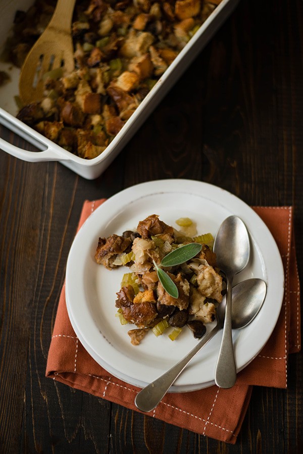 Overhead image of a container of Thanksgiving Stuffing beside a white plate with stuffing and two spoons on it.