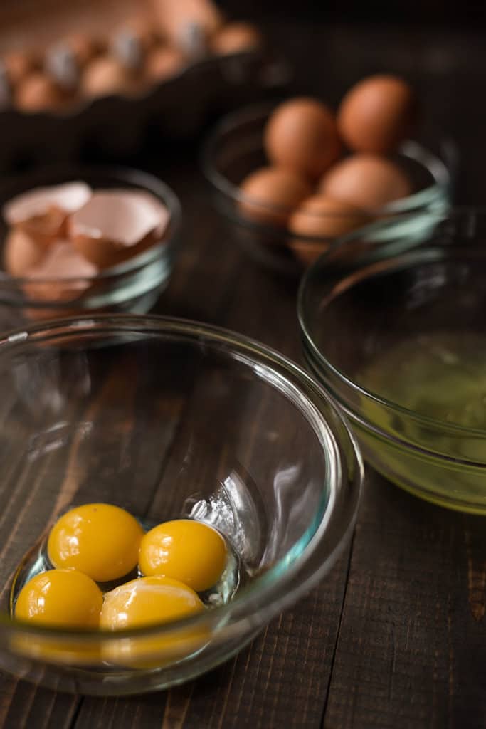 View of a glass bowl containing raw eggs ready to be used in a recipe, with other ingredients in glass bowls nearby.