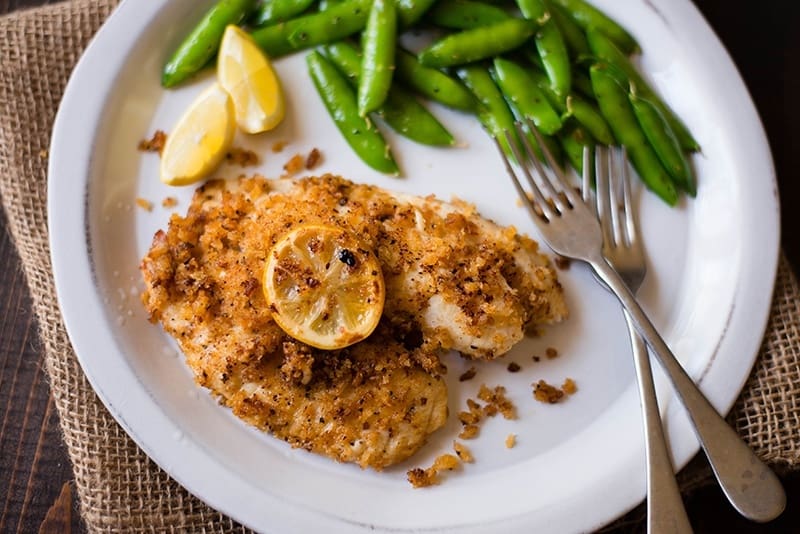 Overhead image of a plate of Panko-Crusted Tilapia, garnished with lemon and served with a side of peas.