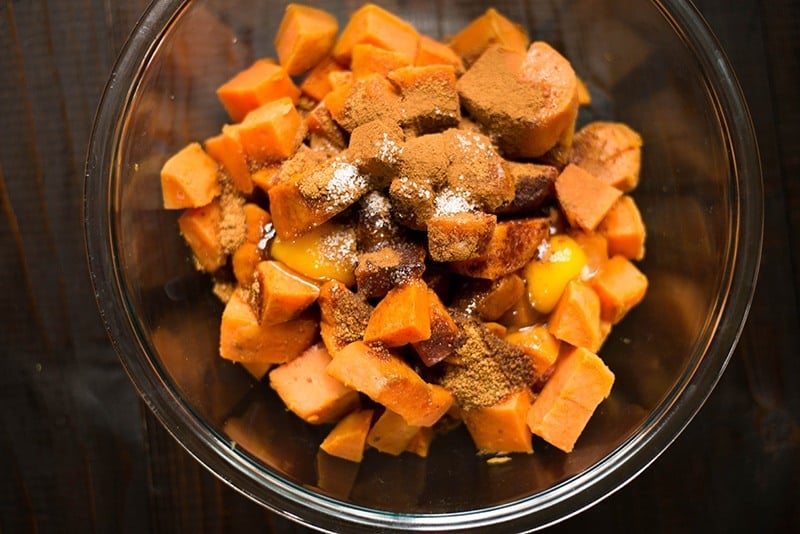 Large mixing bowl filled with the ingredients for the sweet potato filling of the easy sweet potato casserole, including the diced and steamed sweet potatoes, eggs, cinnamon, coconut sugar, salt, ready to be stirred together and slightly mashed.