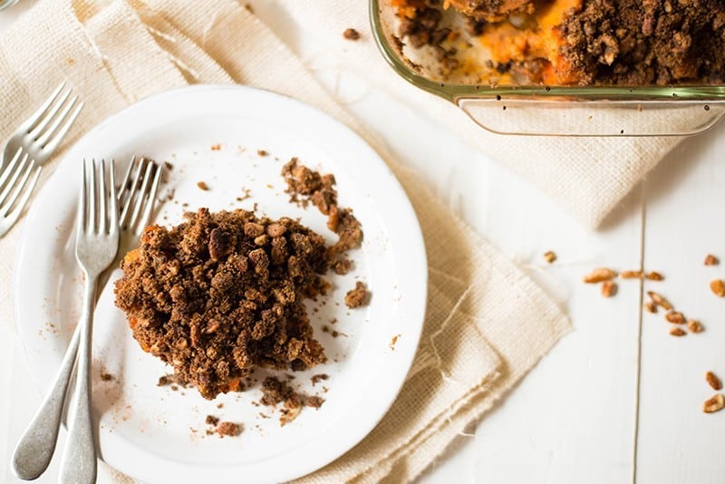 The easy sweet potato casserole that has been set out in an individual portion on a plate. You can see the crumbled pecan topping as well as the baked sweet potato casserole underneath in the casserole dish.