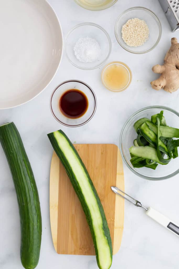Overhead view of ingredients for the Asian cucumber Salad, including Cucumbers, fresh ginger, rice vinegar and sea salt, the cucumbers are partly peeled.