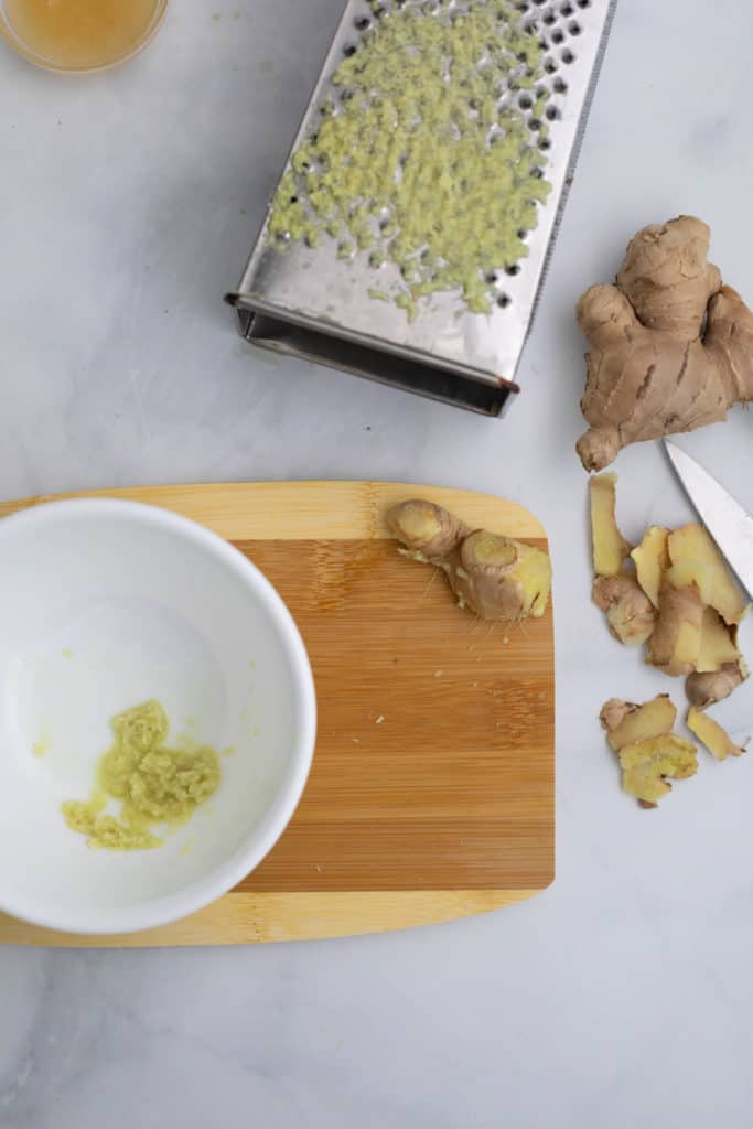 Overhead view of a cutting board, knife, grater, ginger and partially grated ginger.