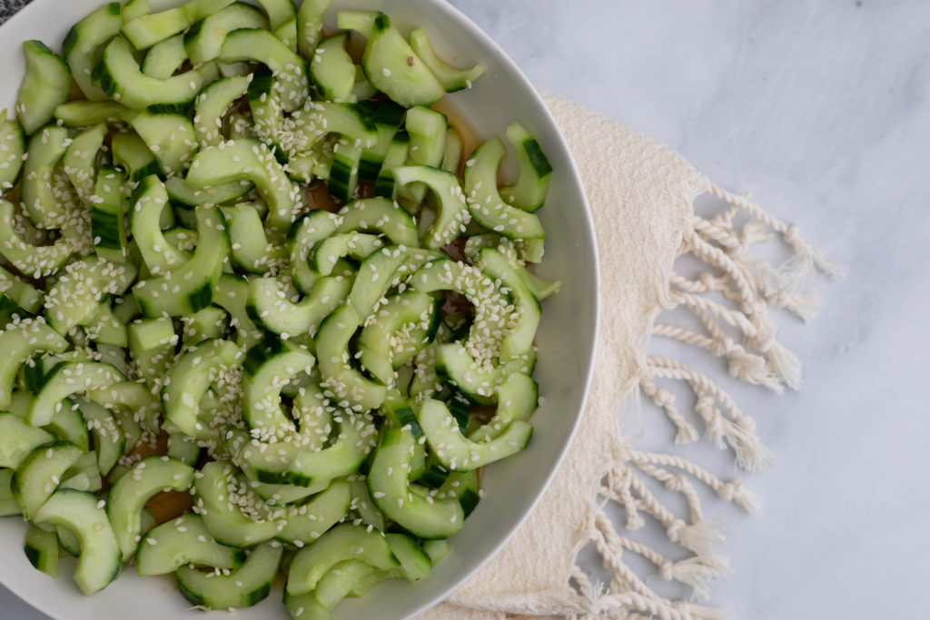 Closeup view of the Asian Cucumber salad in a white bowl, topped with sesame seeds and ready to eat.