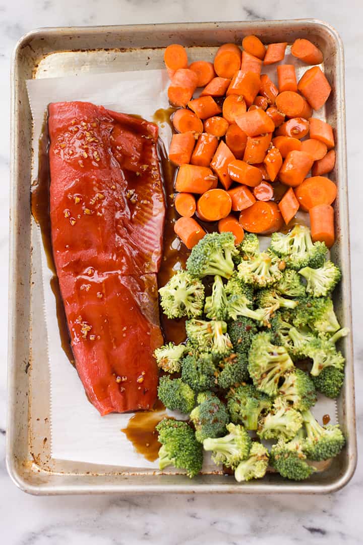 Overhead view of the teriyaki salmon, broccoli, and carrots in rimmed baking sheet before placing into the oven to bake.