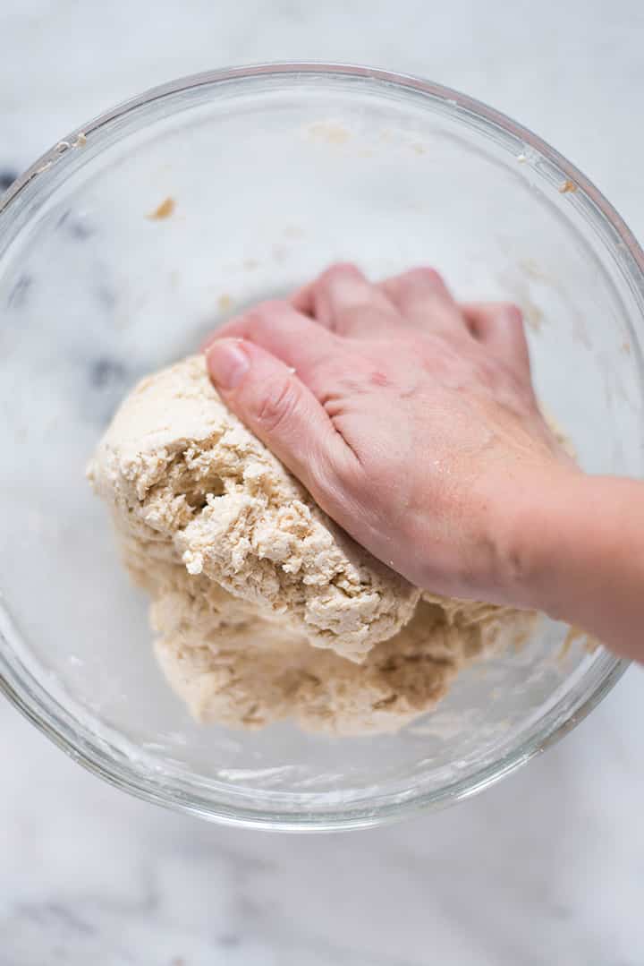 Mixing bowl with homemade bagel recipe dough, being kneaded by hand.