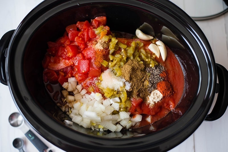 Overhead view of the Crock Pot Shredded Beef Tacos, including ingredients of onions, garlic, tomatoes, chiles, and beef.