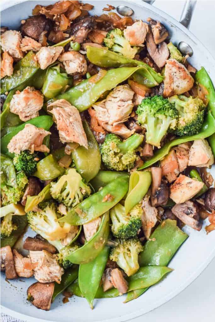 Overhead view of a skillet with the cooked stir fry, including chicken, snow peas, mushrooms, and broccoli.