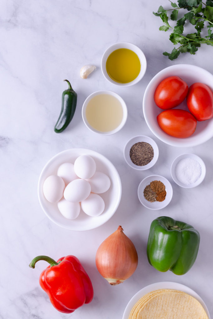 Overhead image of the ingredients for Huevos Rancheros, including bell peppers, onions, spices, corn tortillas and eggs.