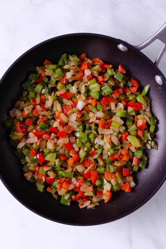 Overhead image of a skillet containing yellow onions, and red and green peppers chopped.