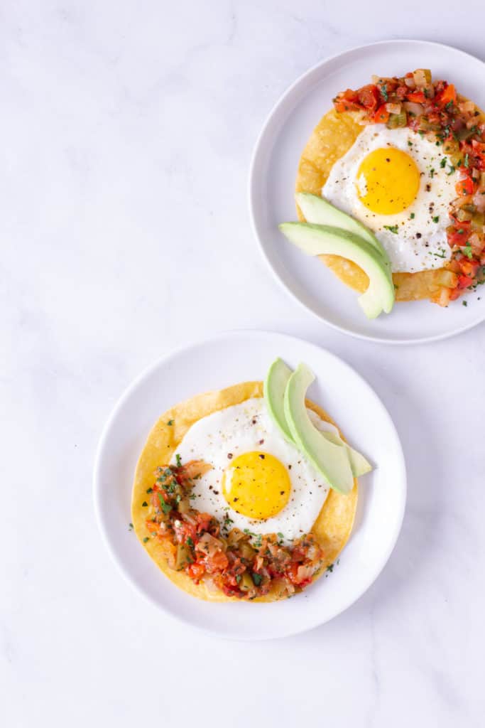 Overhead image of two white plates with Huevos Rancheros, plated and ready to eat, and garnished with avocado.
