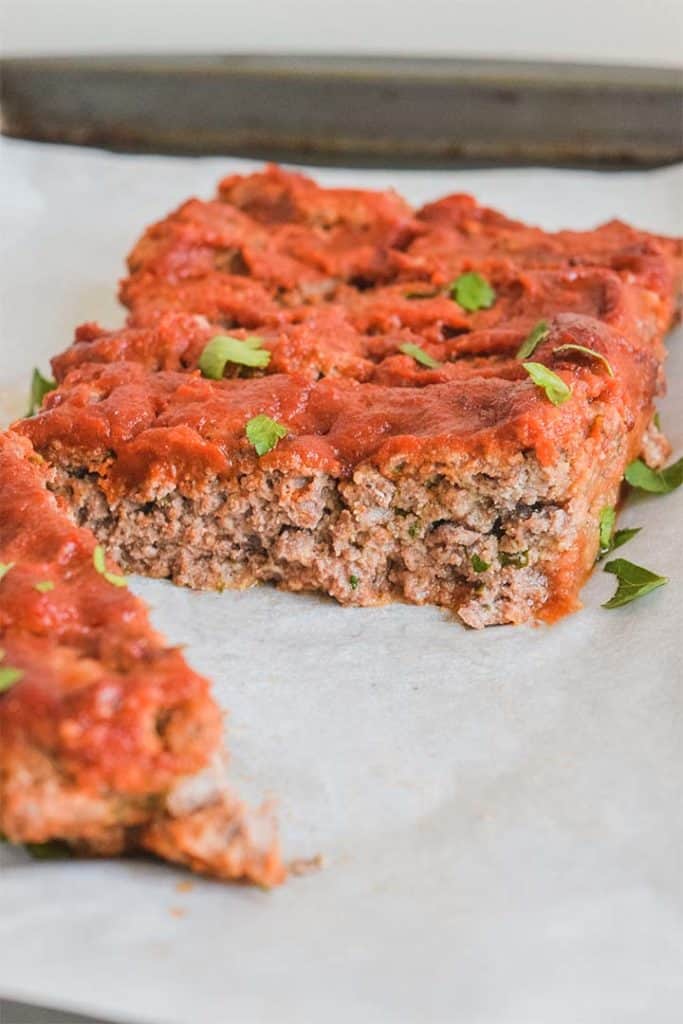 Close up side image of a meatloaf, cut in half on a parchment paper lined sheet. pan.