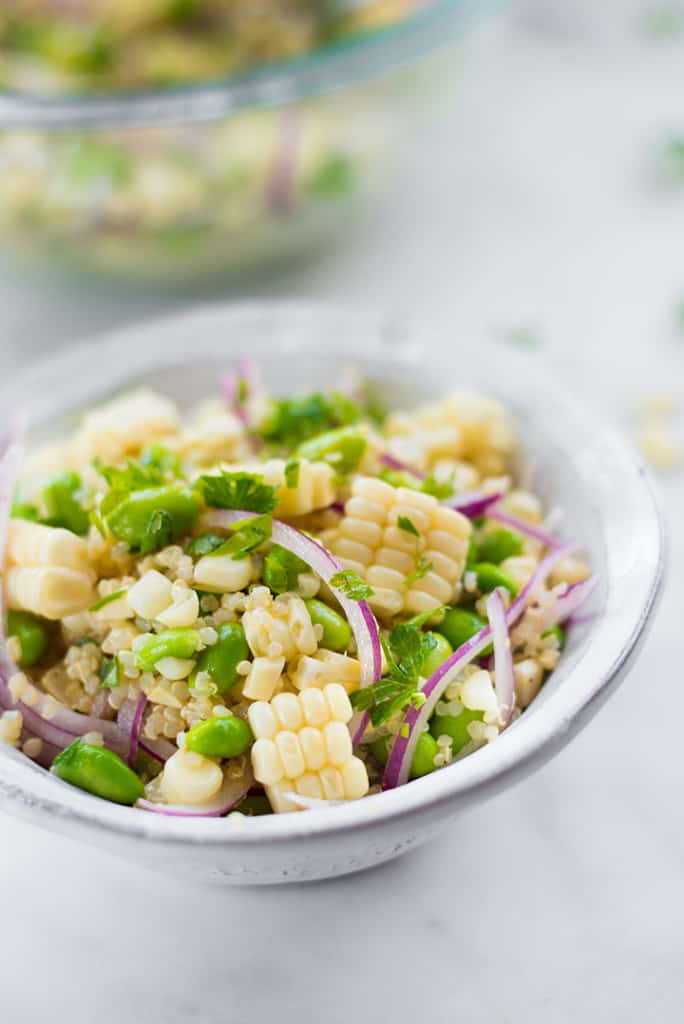 Side view of summer corn edamame salad, filled with cooked quinoa, sliced red onions, edamame, and fresh corn.
