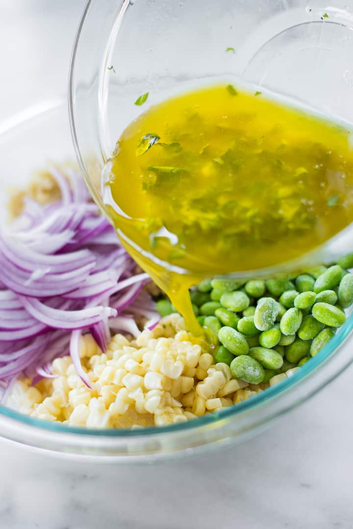 Pouring the lemon basil vinaigrette into the bowl of summer corn edamame salad, which will then be tossed and served. 