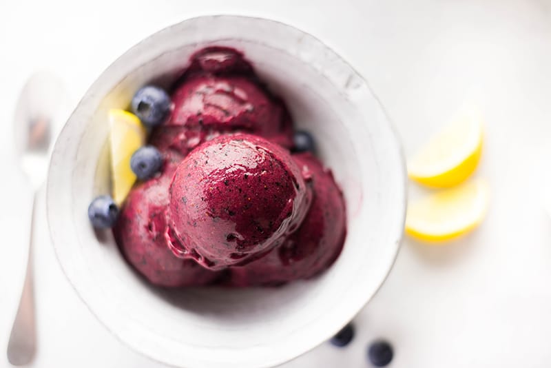 Three scoops of lemon blueberry sorbet, placed in a bowl and garnished with fresh blueberries and thin lemon wedges 