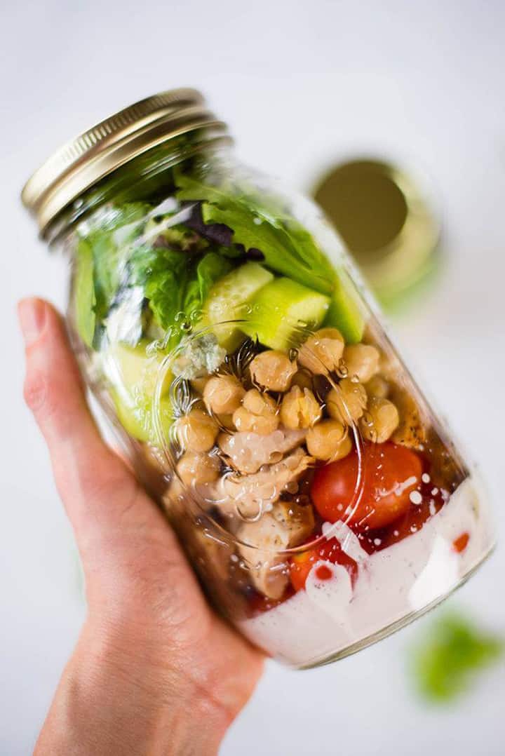 Hand holding a glass Mason jar filled with salad and Greek Yogurt Ranch Dressing.