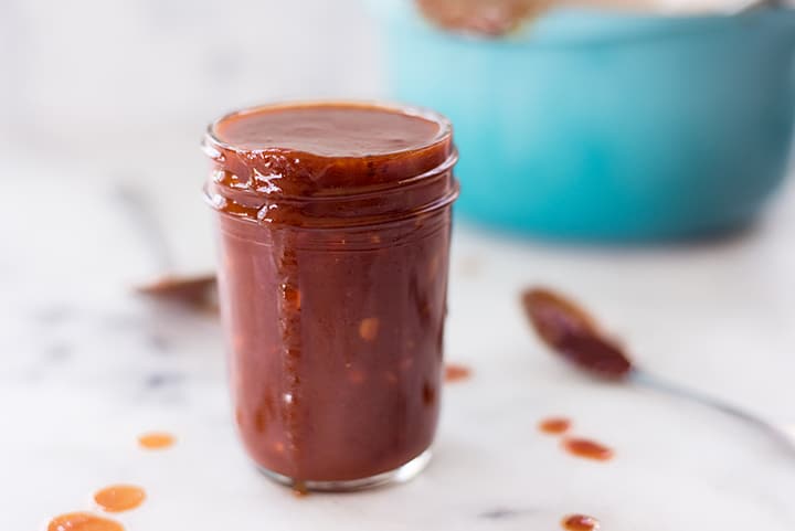 Side view of mason jar filled with sweet bbq sauce which is overflowing.