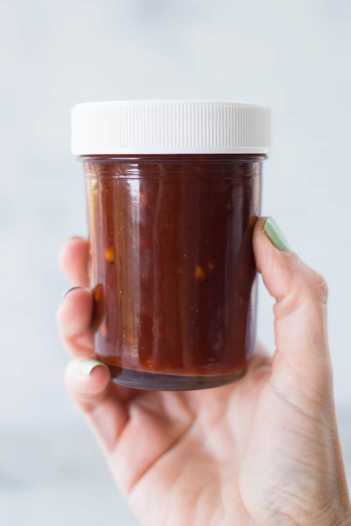 Hand holding a mason jar filled with sweet bbq sauce with a lid for storing bbq sauce in the refrigerator.