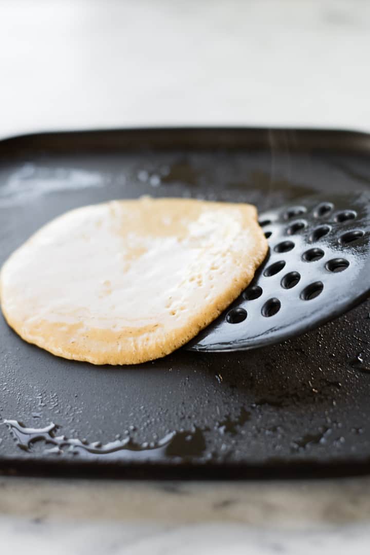 Side image of a Healthy Diner Style Pancake on the griddle being slid onto a spatula, ready to be flipped.