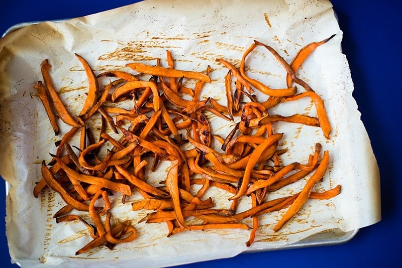 Baked sweet potato fries on a baking sheet, ready to be plated and served. Showing how to make sweet potato fries.