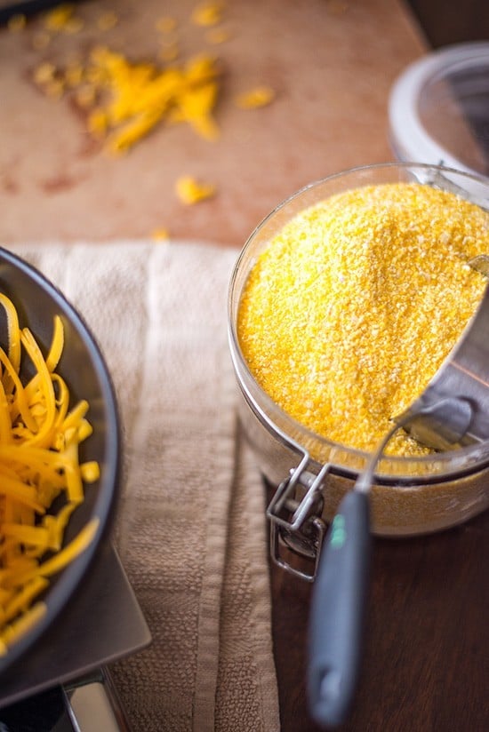 Close up view of a bowl of cornmeal polenta with a measuring spoon in the bowl, and beside it is a bowl of grated cheddar cheese.