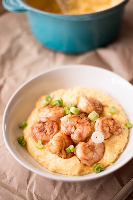 Close up view of a white bowl containing Healthy Shrimp and Grits, with a blue pot of grits in the background.