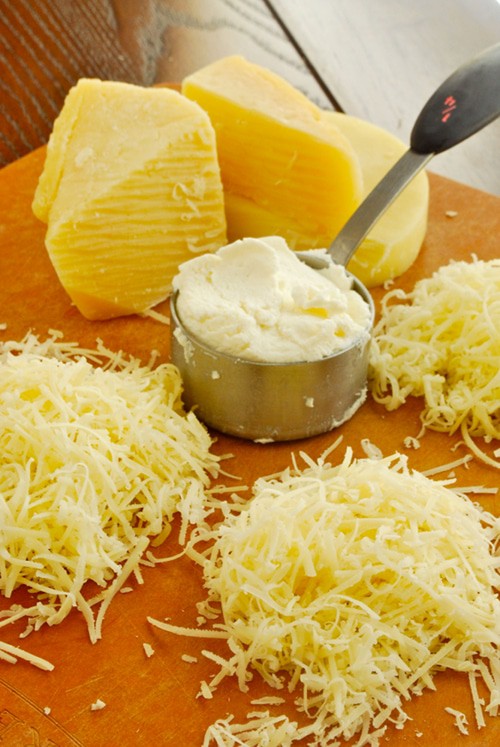 Close up image of various types of cheeses, some grated, some shredded, and two pieces in blocks as examples of healthy saturated fat.