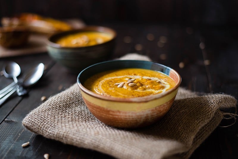 Horizontal image of a bowl of butternut squash bisque that has been topped with additional cream and butternut squash seeds.