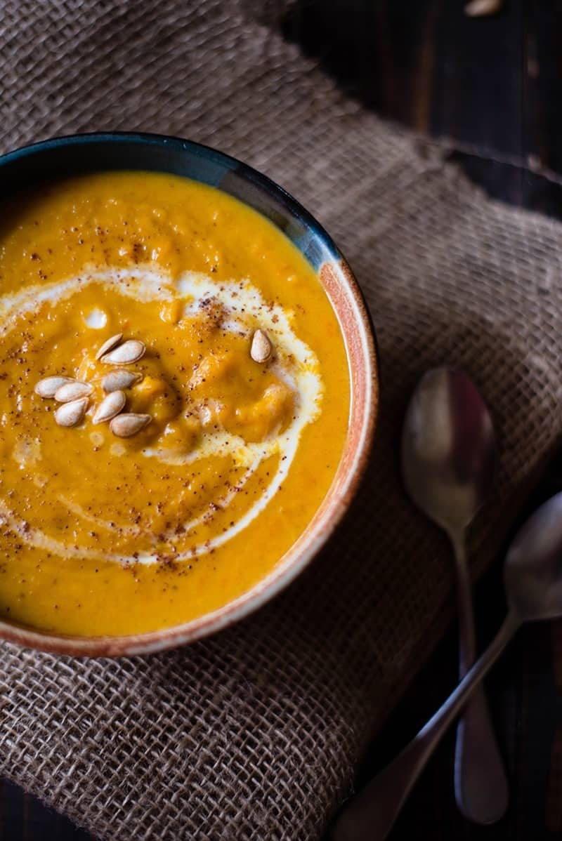 Close up of a bowl of butternut squash bisque that has been garnished with roasted butternut squash seeds, cream, and ground nutmeg.