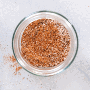 A clear bowl of seasoning salt, with a little sprinkled on the light marbled countertop.
