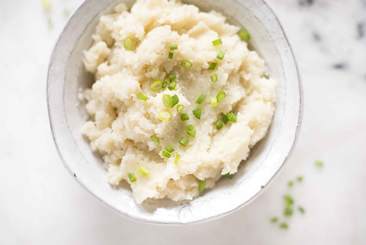 Horizontal image of the cauliflower mashed potatoes that are garnished with sliced chives.