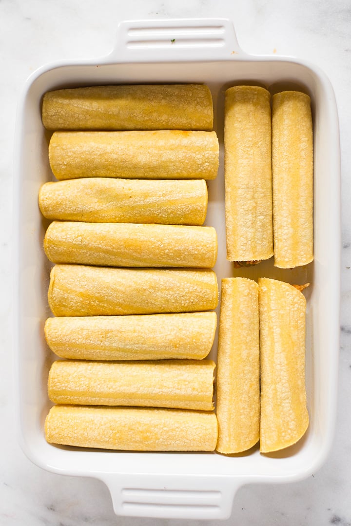 Overhead view of a casserole dish which is filled with the stuffed shredded chicken enchiladas that have been wrapped in corn tortillas and are ready to be topped with the enchilada sauce and cheese and then baked.