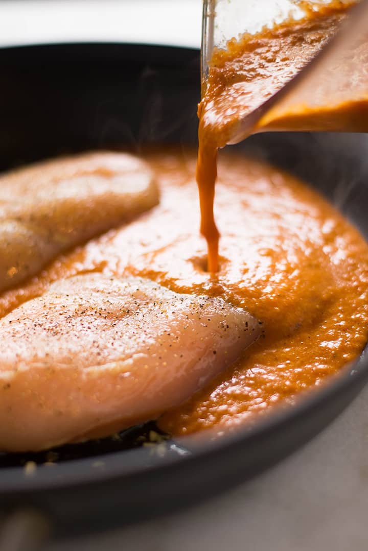 Side angle of pouring the homemade enchilada sauce over the chicken into the skillet to make the shredded chicken for the shredded chicken enchiladas.