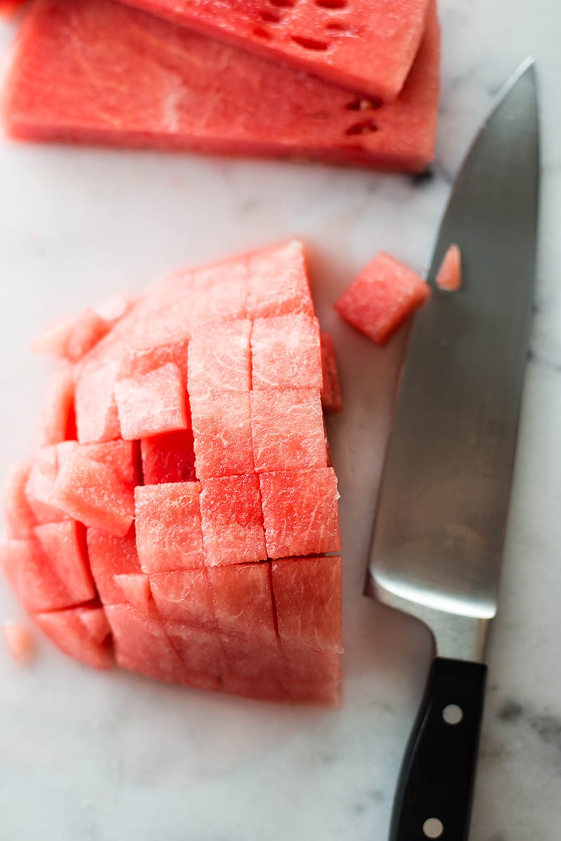 Overhead image of sliced and chopped watermelon, with a large knife beside the watermelon.