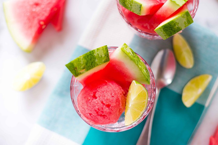 Close-up image of watermelon sorbet, ready to eat, with fresh watermelon and lime wedges sitting next to it