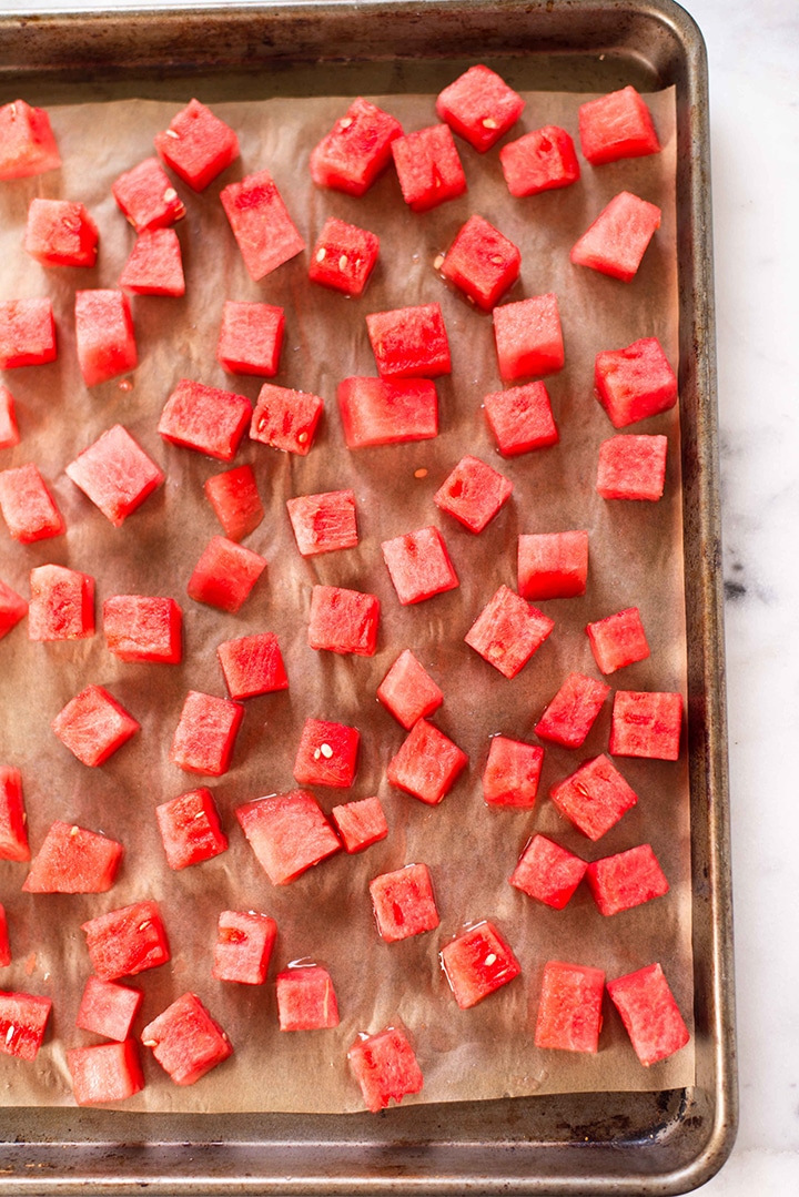 Diced watermelon without the rind laying on a baking sheet lined with parchment paper, ready to freeze to be turned into watermelon sorbet.