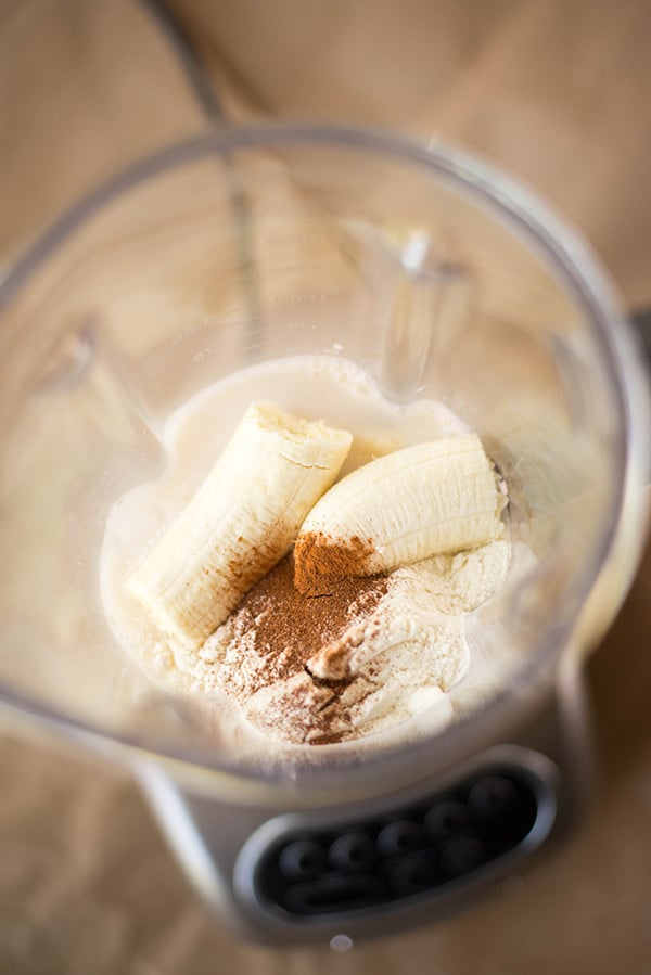 A chopped frozen banana, cinnamon, almond milk, and vanilla protein powder placed in a blender, ready to make a banana protein shake 