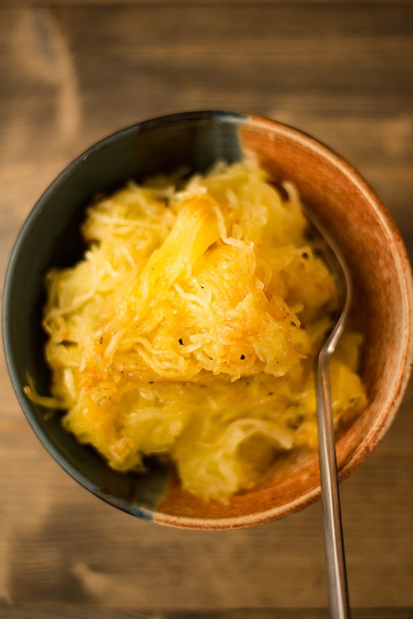 Single bowl of spaghetti squash noodles with a fork, and seasoned with sea salt and black pepper, ready to eat.