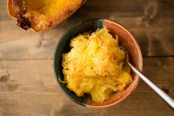 Bowl of spaghetti squash noodles that have been seasoned with sea salt and black pepper, next to a baked spaghetti squash.