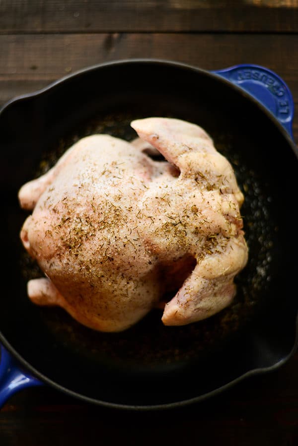 Overhead image of a blue oven-proof skillet containing a prepped roasted chicken for the Healthy Oven Roasted Chicken Recipe.