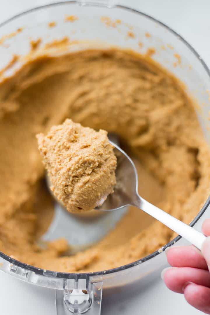Overhead view of a spoon scooping out of a food processor, the fully blended Honey Roasted Peanut Butter.
