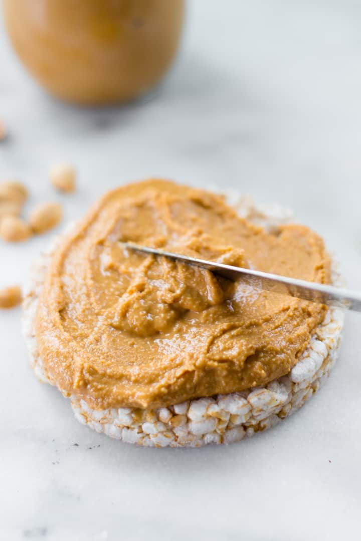 Close up view of homemade honey roasted peanut butter being spread on a rice cake as a food to lower blood sugar.