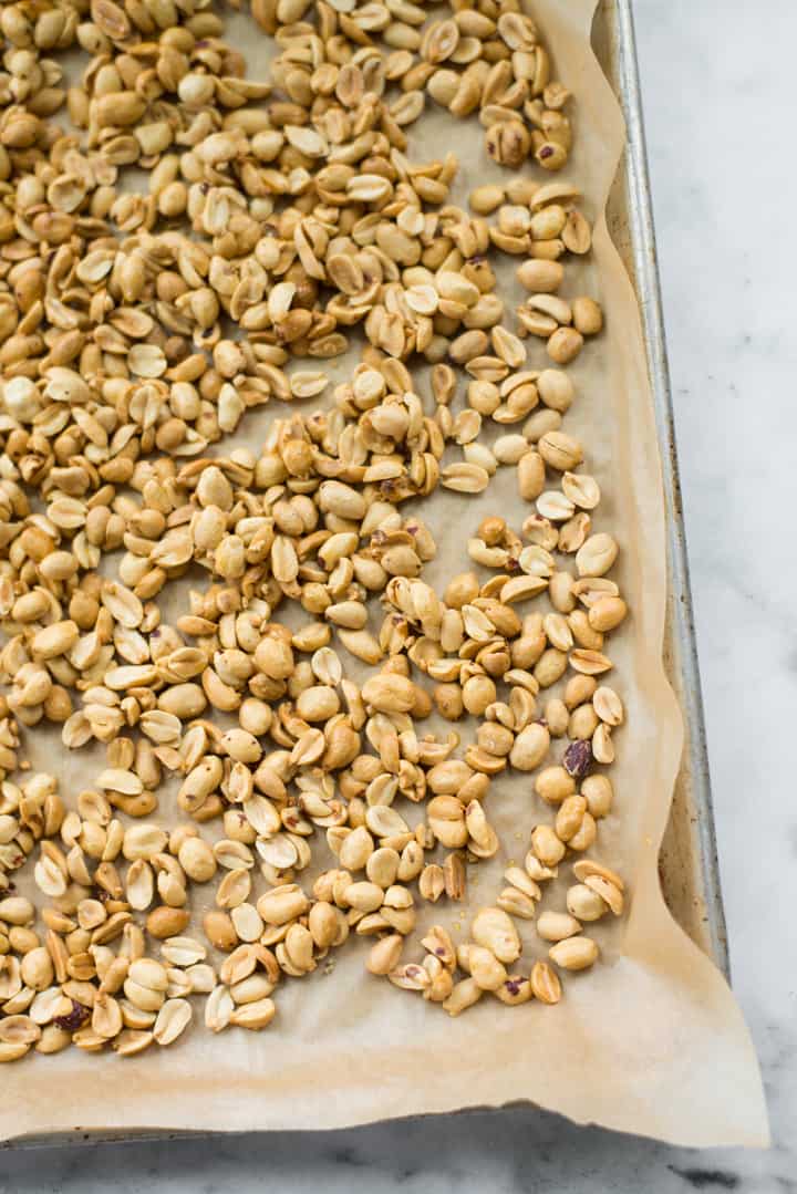 Overhead image of raw honey and salt covered roasted peanuts, coming out of the oven as preparation for Honey Roasted Peanut Butter.
