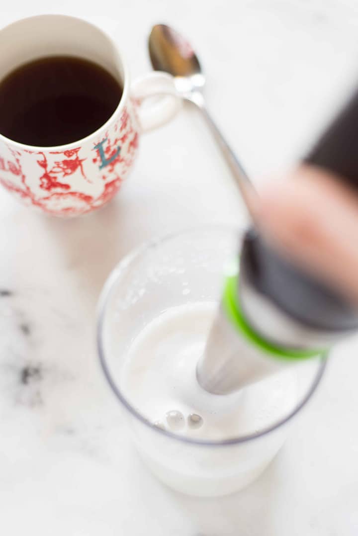 Beaker filled with warmed milk that is being emulsified and frothed to make the milk for a homemade latte using an immersion blender.