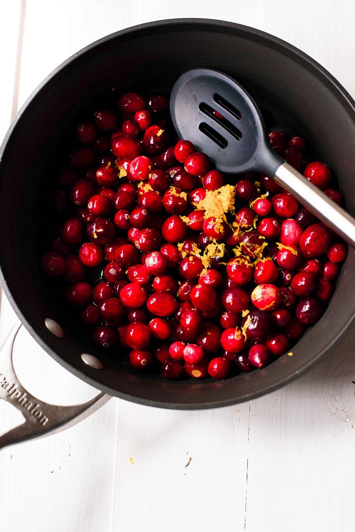 Overhead view of all four ingredients, the fresh cranberries, orange zest, raw honey, and orange juice, are in a sauce pan to be cooked down to make the best homemade cranberry sauce.