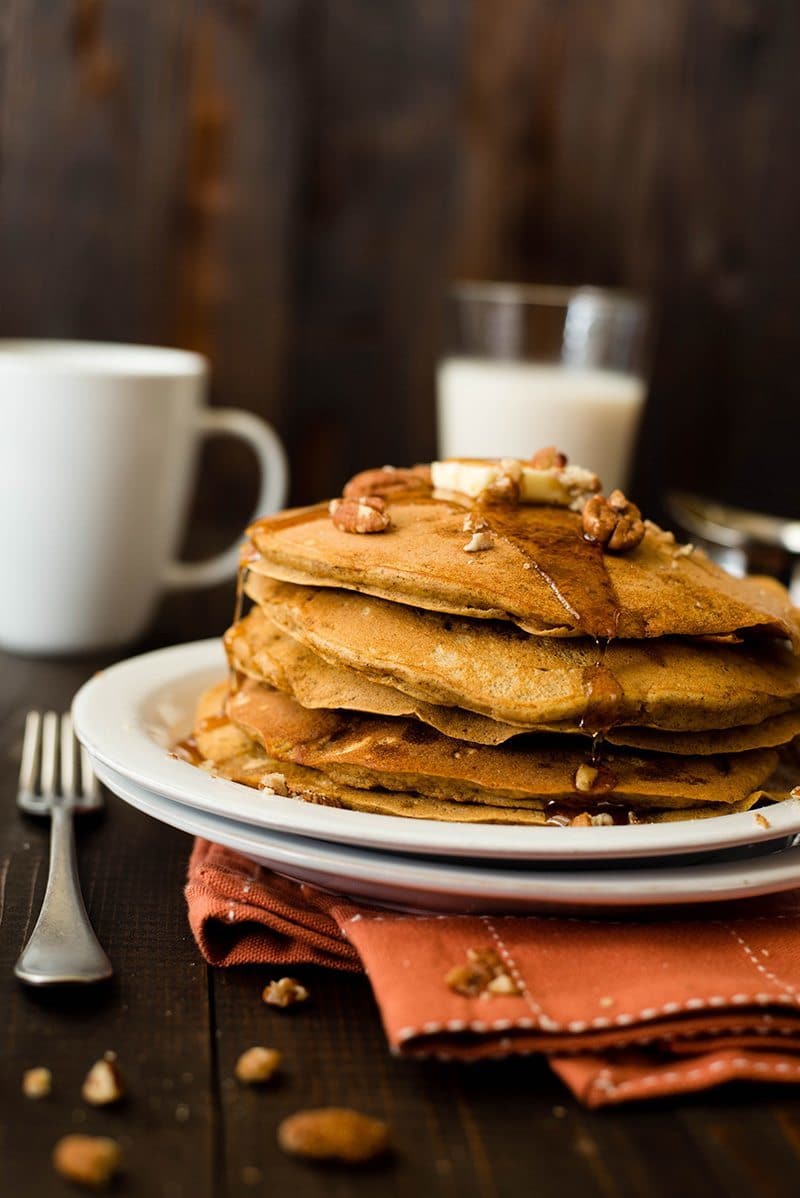 View of a stack of Healthy Pumpkin Pancakes covered in pure maple syrup, with a glass of milk in the background